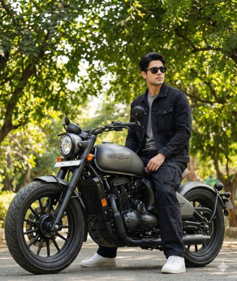 Gemini Ai Generated Image: A man wearing a black denim jacket and black pants is sitting on a matte grey motorcycle (a Jawa bike) outdoors in a tree-lined area. He is wearing sunglasses and white shoes.